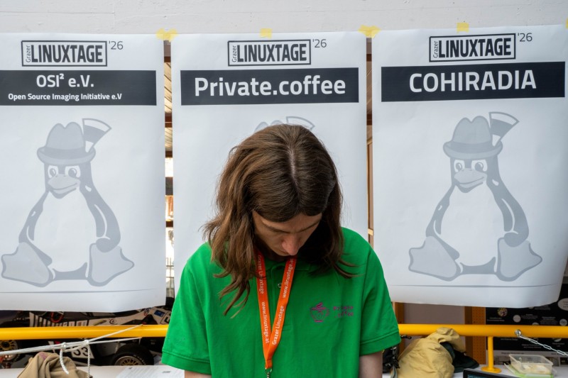 Kumi is working on some private.coffee related service looking down at a laptop with a sign that reads "private.coffee" in the background